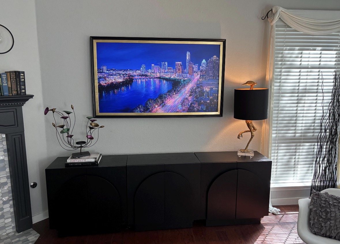 TV with a dark frame and gold inner edge, displaying a blue city skyline above a black console.