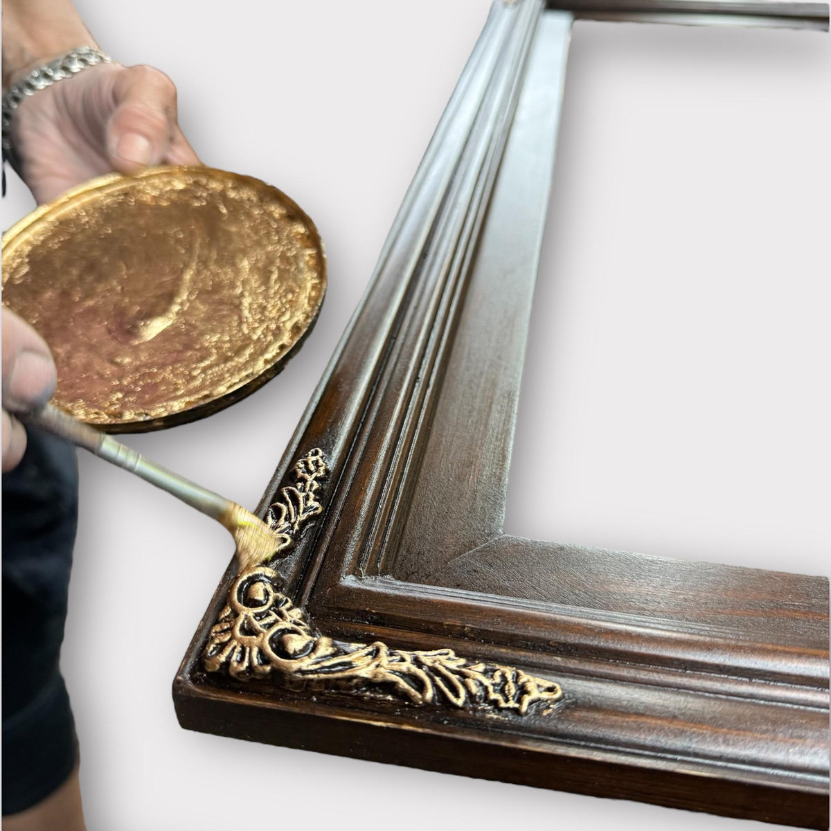 An artisan hand-painting the ornamental details of a wood frame