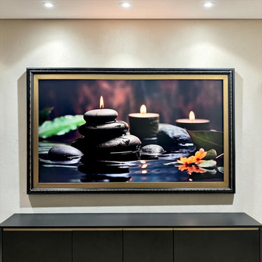 A framed photograph of a serene scene with a stack of stones, lit candles, and a flower, all set against a dark background.