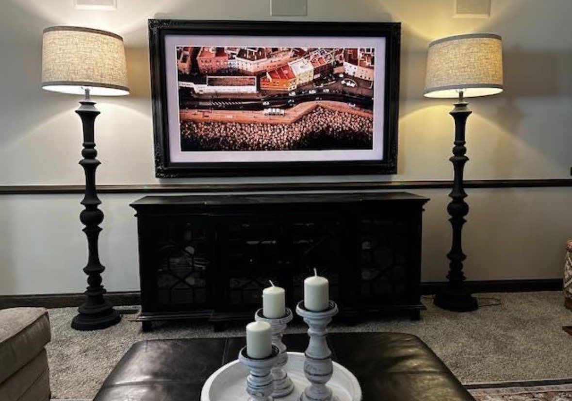 Framed TV above a dark console, with matching lamps on either side.